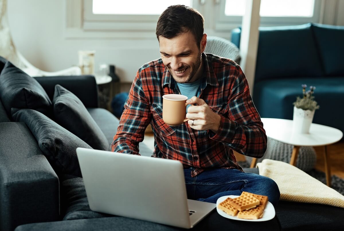 A man who looks a little like Nicholas Hoult in a beard is sitting at a laptop. He has coffee and waffles for breakfast and is smiling because he’s enjoying browsing Usenet with a secure SSL connection.