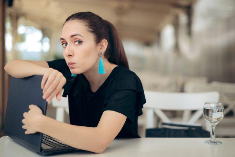 Do I need a VPN for Usenet? A woman wearing a black shirt and long, teal-colored, tasseled earrings is looking at the camera and using her arms to shield her laptop screen from view.