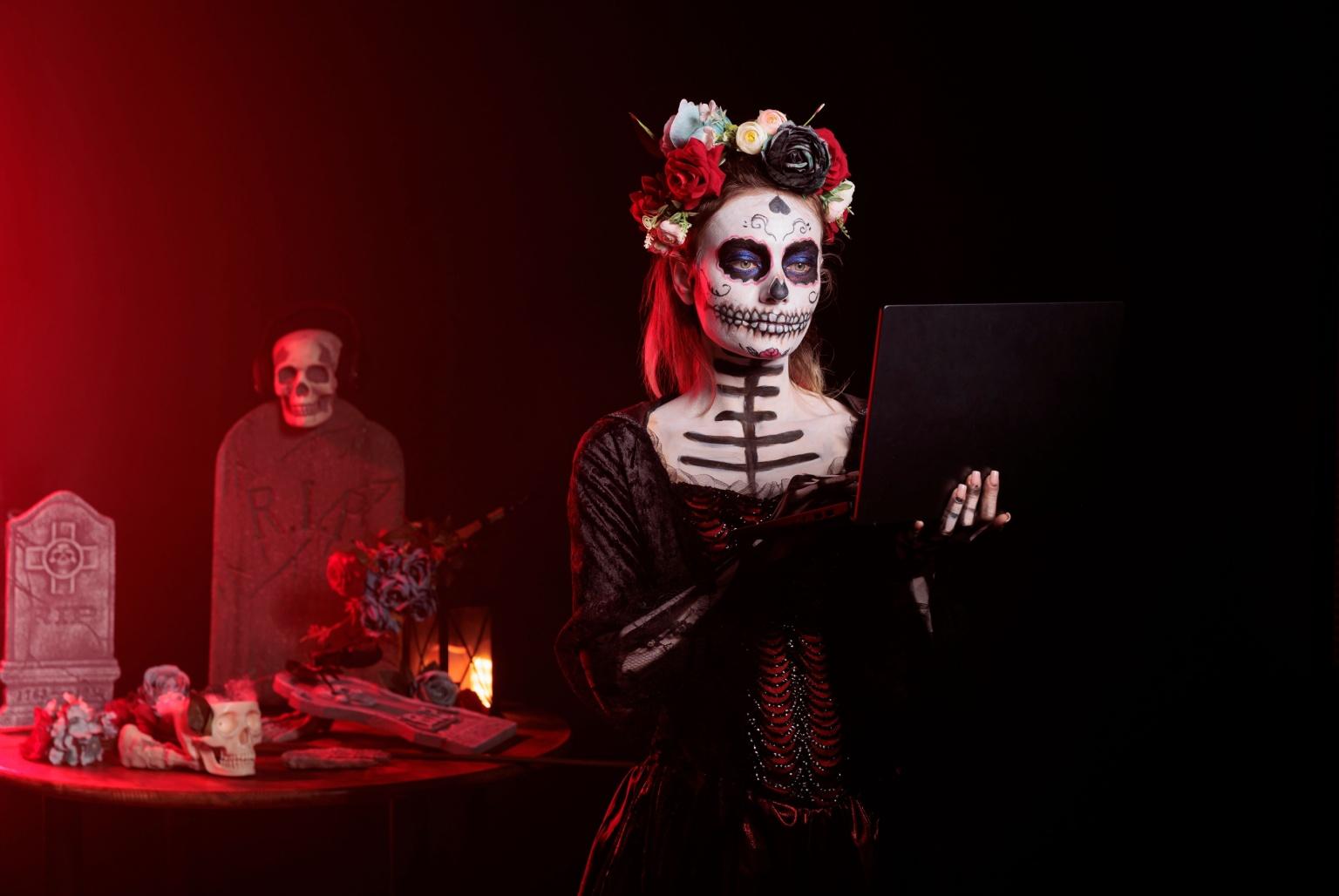 Is Usenet Dead? A woman is dressed like La Catrina, her face and chest designed to look like a sugar skull. She is holding a laptop, answering the question "Is Usenet dead?" In the background is a couple of grave stones and a skull wearing headphones.